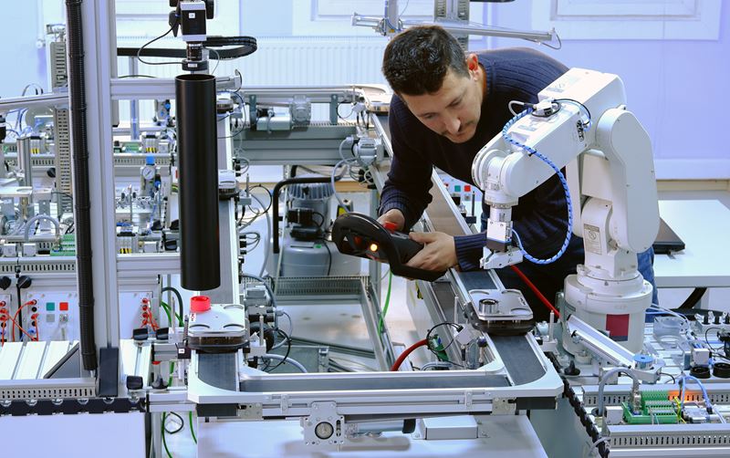 A man is programming a robotic arm in a factory
